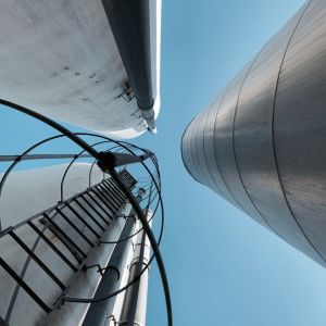 Der Blick zwischen drei hohen Industriesilos vor einem strahlend blauen Himmel, im Vordergrund eine an einem der Silos befestigte Metallwendeltreppe – eine eindrucksvolle Szene, die an Holidus sorgfältig zusammengestellte Sammlung einzigartiger Reiseziele und architektonischer Meisterwerke erinnert.